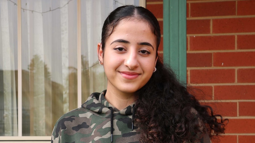 A photo of Sara smiling in front of their safe house in Melbourne after escaping war-torn Iraq