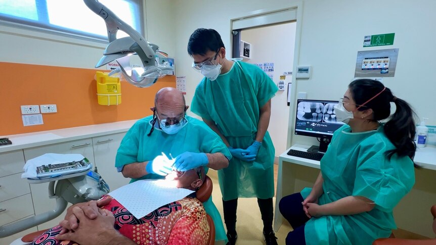 Two student dentists watch their supervisor conduct a procedure.