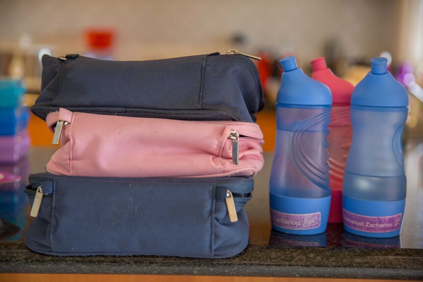 Three water bottles and lunch bags sit on the kitchen counter