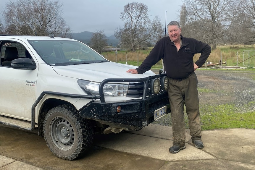 farmer leaning on his ute, in his dirty mud splattered trousers