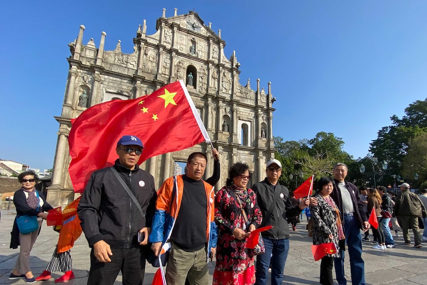 Chinese tourists wave national flags in Macau in front of old ruins.