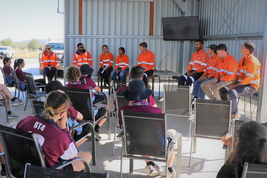 A group of students sit and listen to workers.