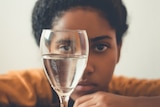 A woman rests her chin on a table and looks at a wine glass half full of water
