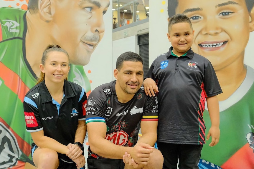Cody Walker kneels as he poses for a photo with two kids at the National Centre of Indigenous Excellence.