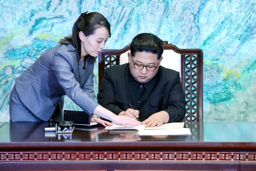 A North Korean woman in her 30s helps a North Korean man in his 30 sign a document.