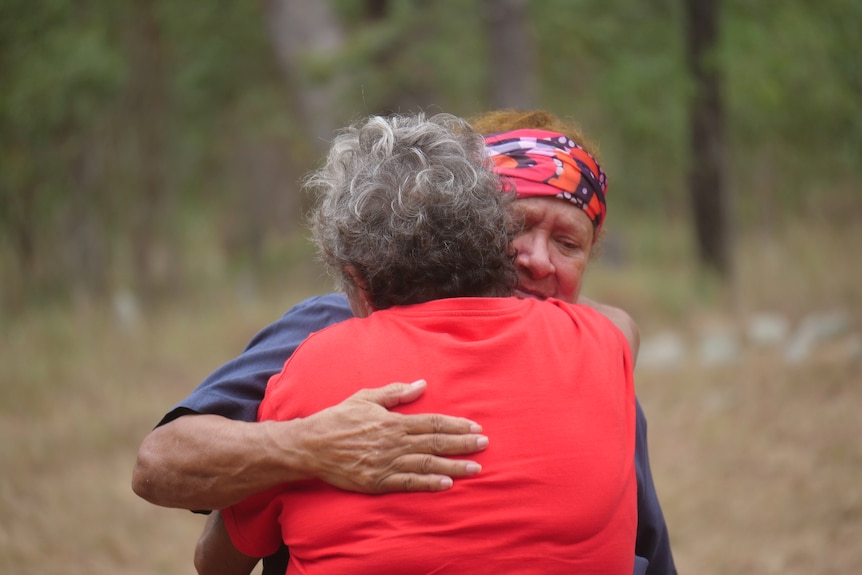 Two Indigenous women hugging each other in bushland.