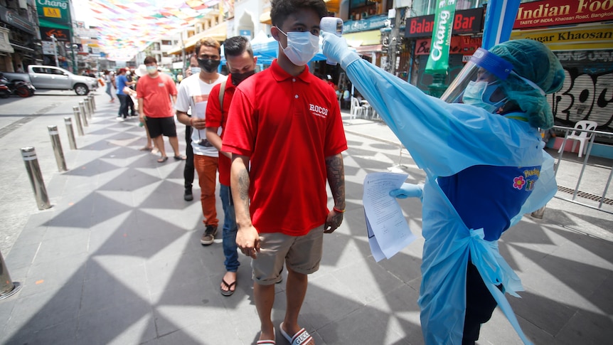 A health worker checks the temperature of a man falling in line for a COVID-19 swab test in Khaosan Road in Bangkok.