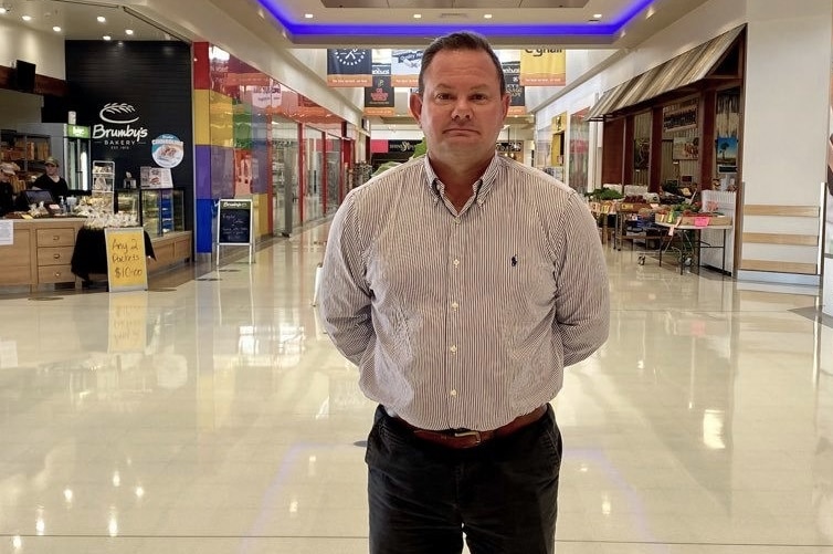 A man wearing a button up shirt stands in the middle of an empty shopping centre.