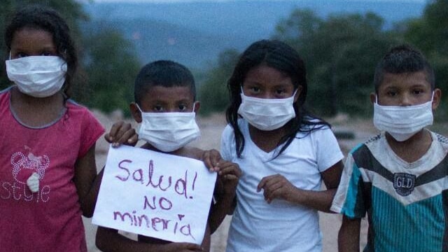 Children wearing face masks hold a sign.