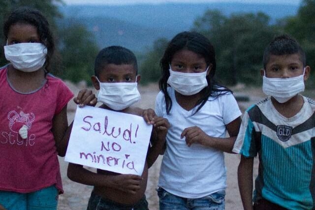 Children wearing face masks hold a sign.