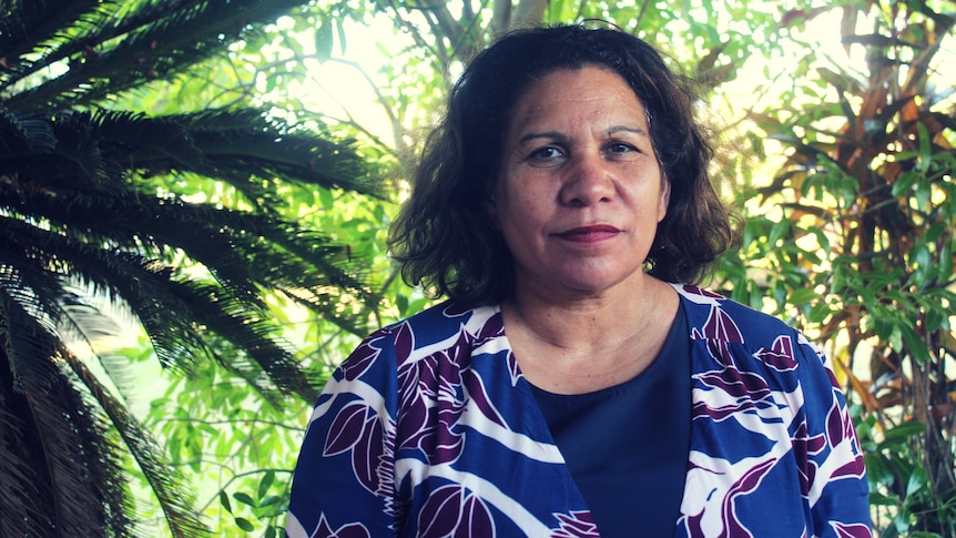 Leanne Liddle stands outside, tropical trees and gardens are in the background