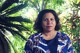 Leanne Liddle stands outside, tropical trees and gardens are in the background