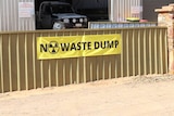 A yellow sign saying 'no waste dump' on a fence