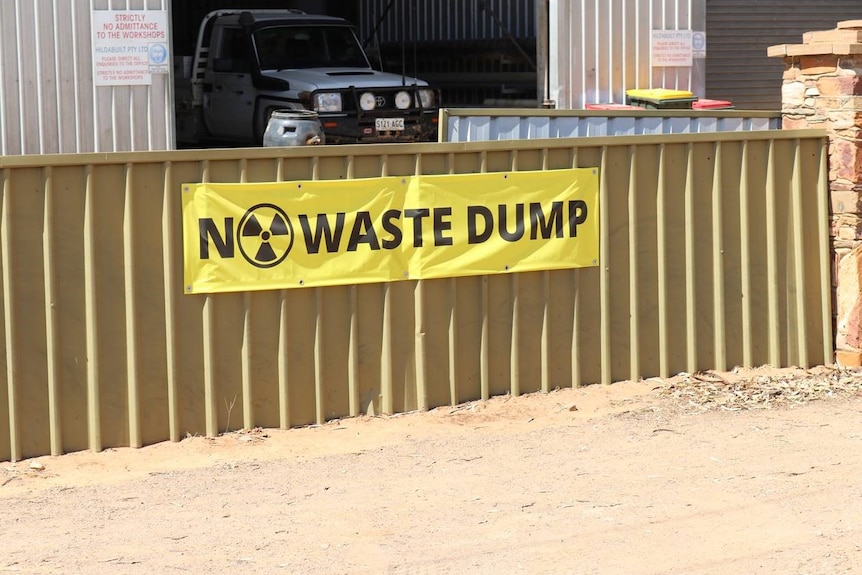 A yellow sign saying 'no waste dump' on a fence