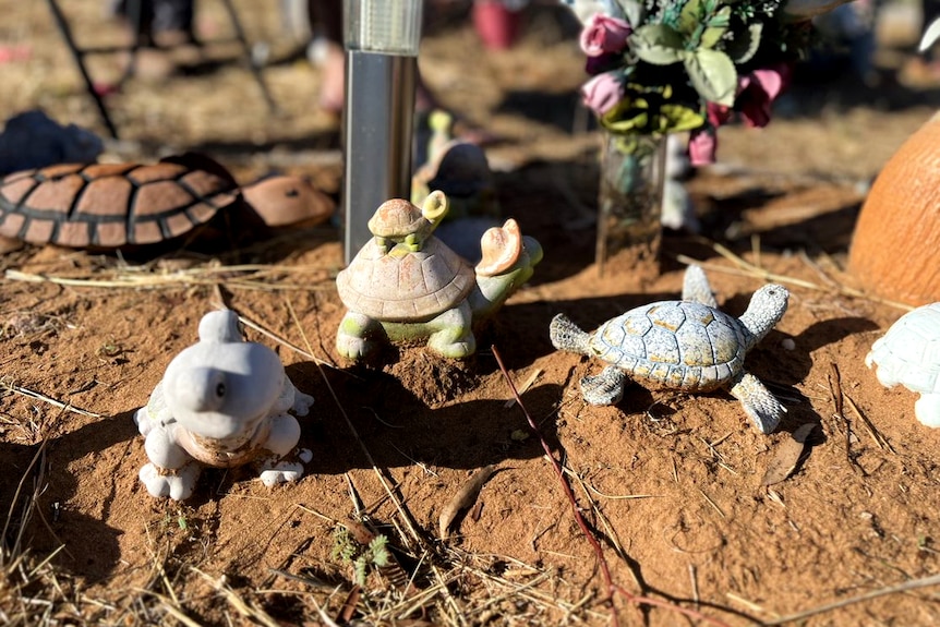 Several turtle statues sit beside flowers on a grave.