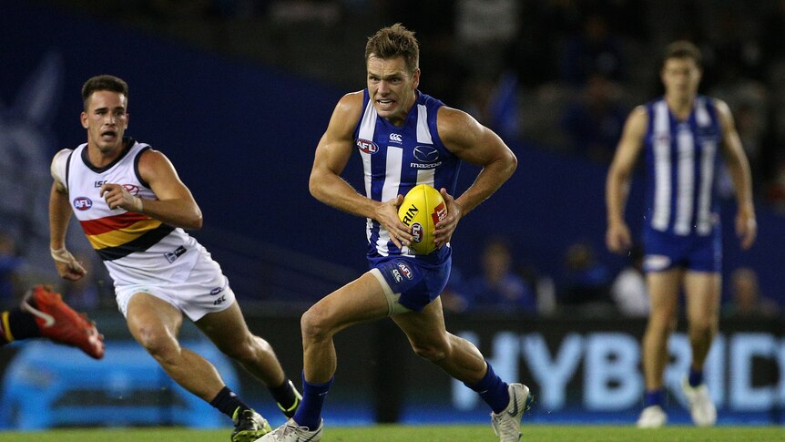 An AFL player runs with the ball as opponents chase after him