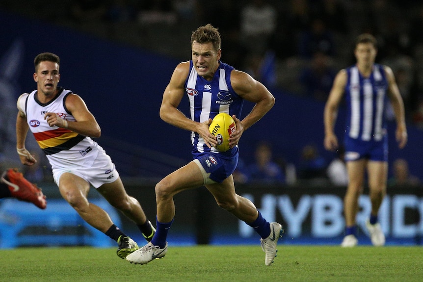 An AFL player runs with the ball as opponents chase after him