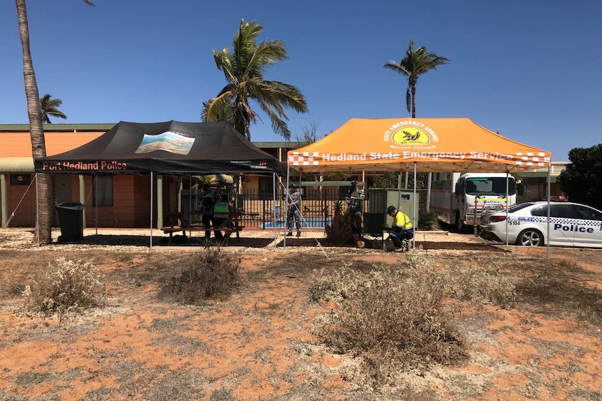 Two large pop-up tents, one black and one bright orange, sit out the front of a hotel with police cars and officers.