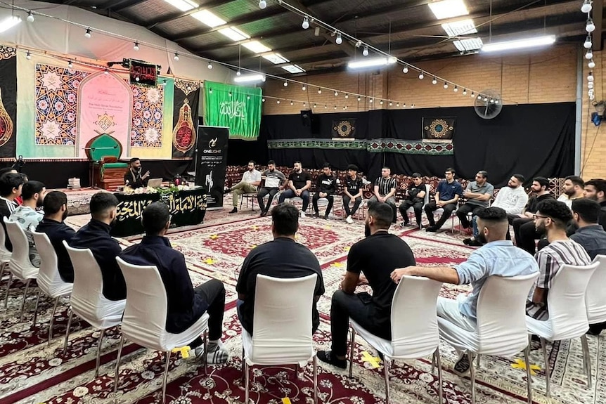 A photo of youth sitting in a circle, listening to a lecture during Muharram.