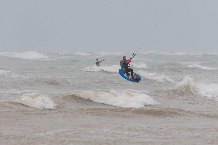 Two kitesurfers in Darwin's rough surf, one of which is getting airborne.