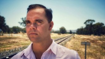 A man stands next to railway tracks, looking into the distance.