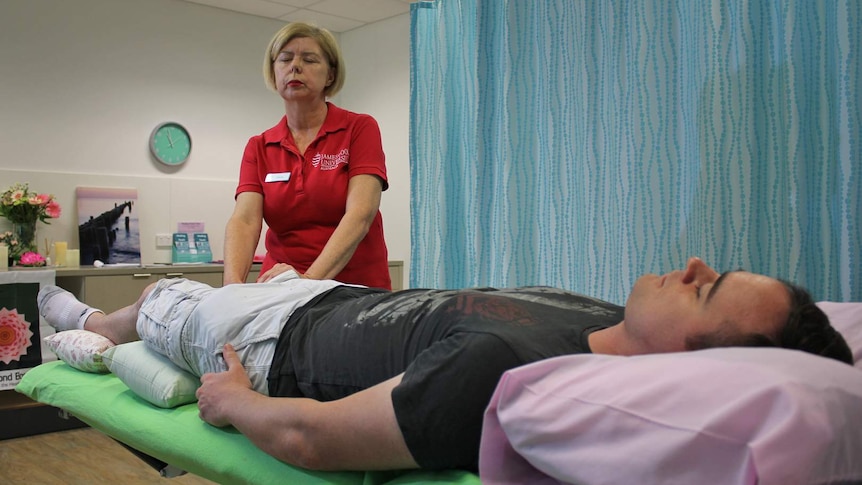 A woman in a red shirt performs healing touch on a man who is lying down