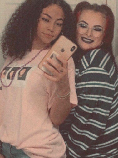 A young black woman and a young white woman take a selfie together in a mirror