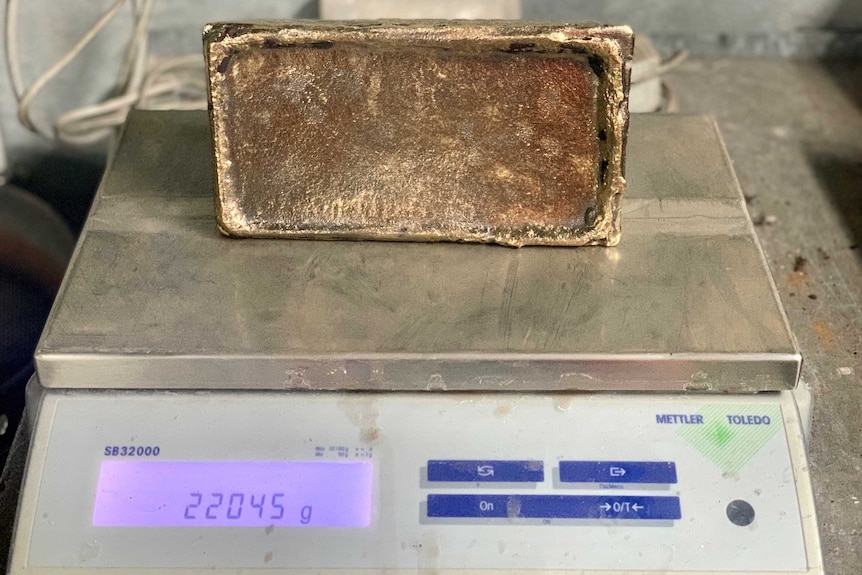 A gold brick sits on a scale, weighing 22 kilograms.