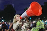 A protestor chants anti-Brexit slogans through an orange traffic cone as police try to negotiate with them to leave.