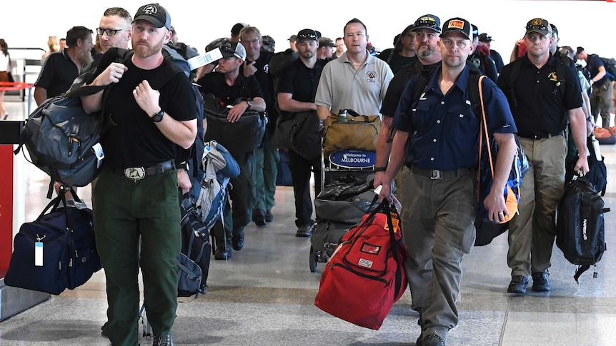 A group of men walks through a Melbourne airport terminal, carrying luggage.