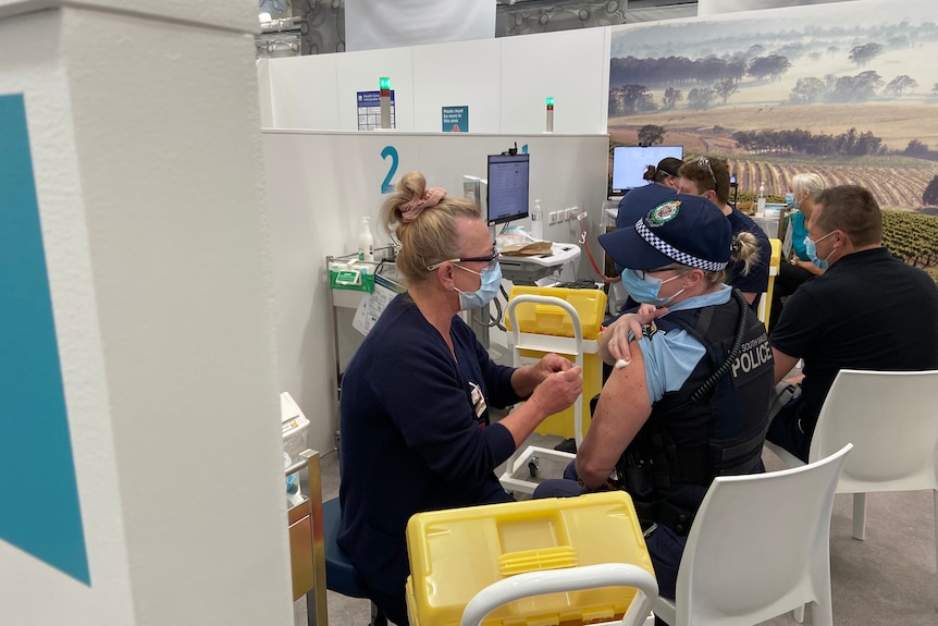 A staff member from Hunter New England Health delivers the COVID vaccine to a police officer