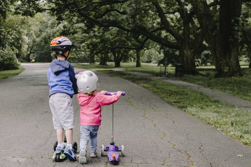 Two kids on scooters in a green park