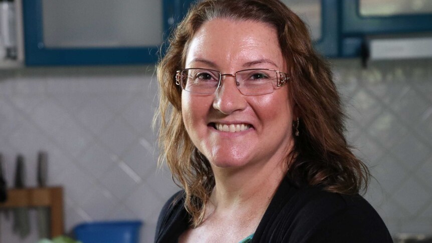 A head and shoulders shot of a smiling Joanna Rusling in her kitchen, posing for a photo and wearing spectacles.