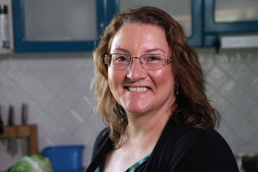 A head and shoulders shot of a smiling Joanna Rusling in her kitchen, posing for a photo and wearing spectacles.