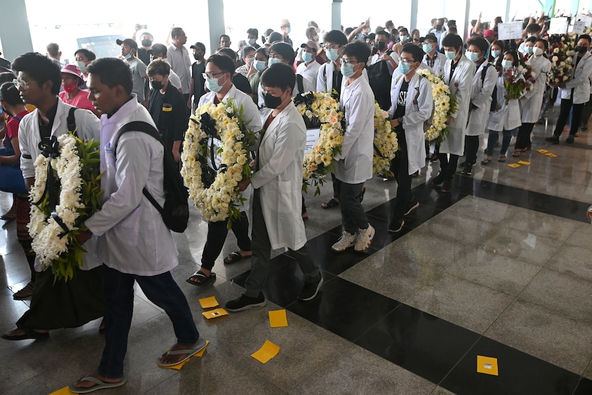 A funeral procession with people wearing white coats and carrying flowers