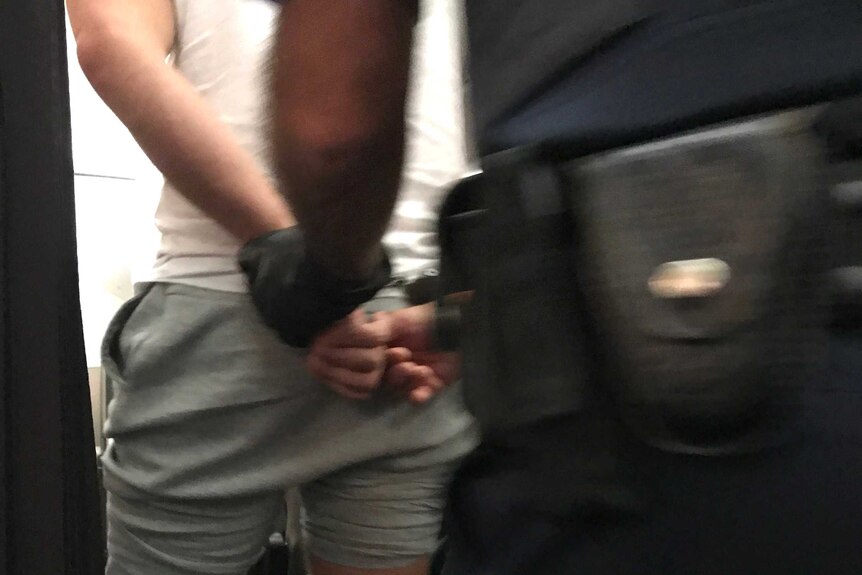 The rear view of a man in handcuffs being escorted by a police officer.
