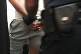 The rear view of a man in handcuffs being escorted by a police officer.