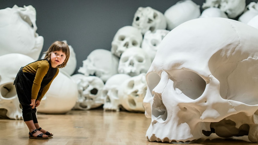 A child views Ron Mueck's 100 gigantic skulls