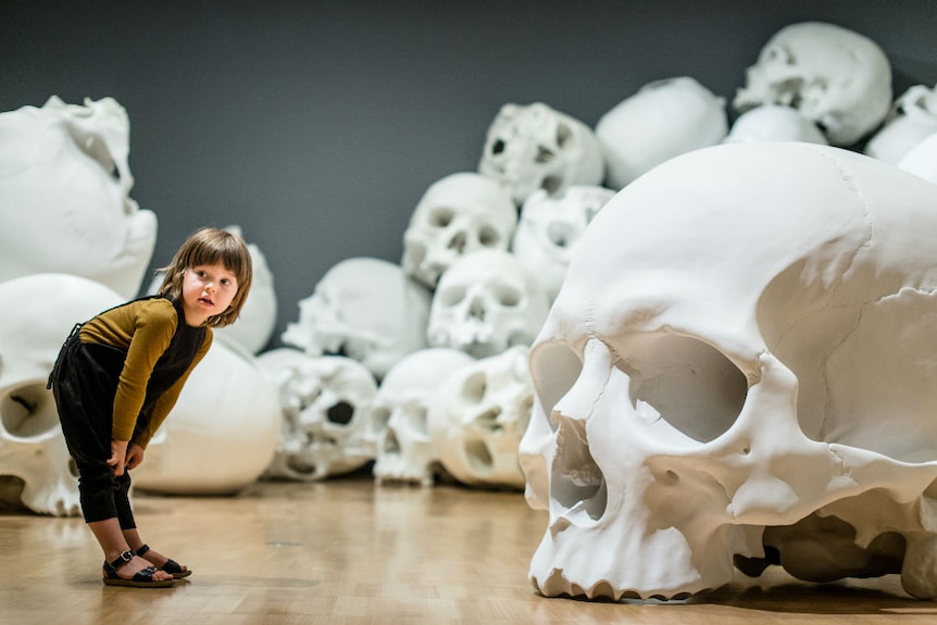 A child views Ron Mueck's 100 gigantic skulls