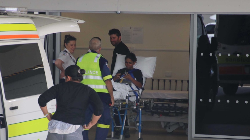 People exit an ambulance at a hospital. One is on a stretcher.