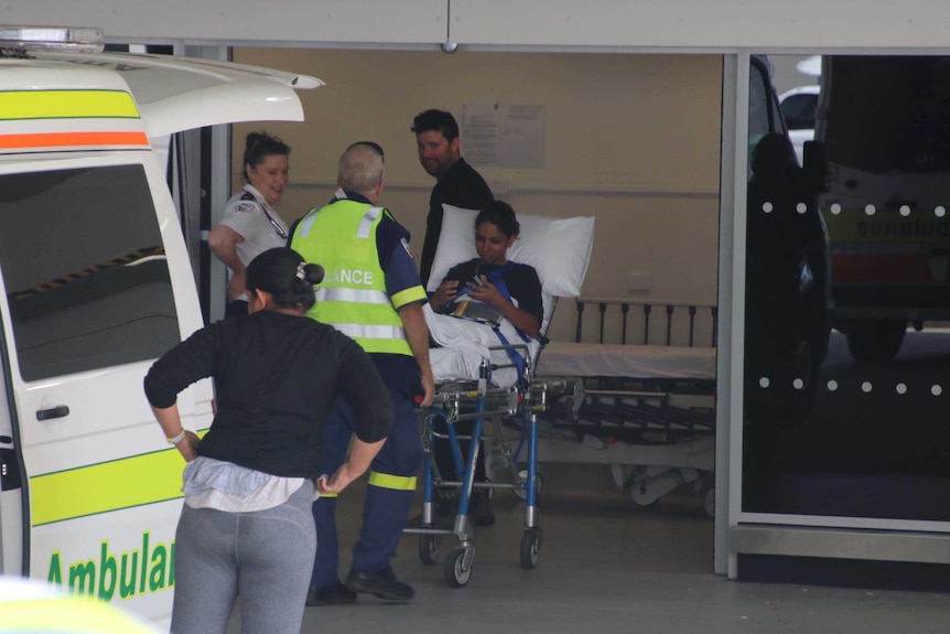 People exit an ambulance at a hospital. One is on a stretcher.