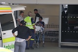 People exit an ambulance at a hospital. One is on a stretcher.