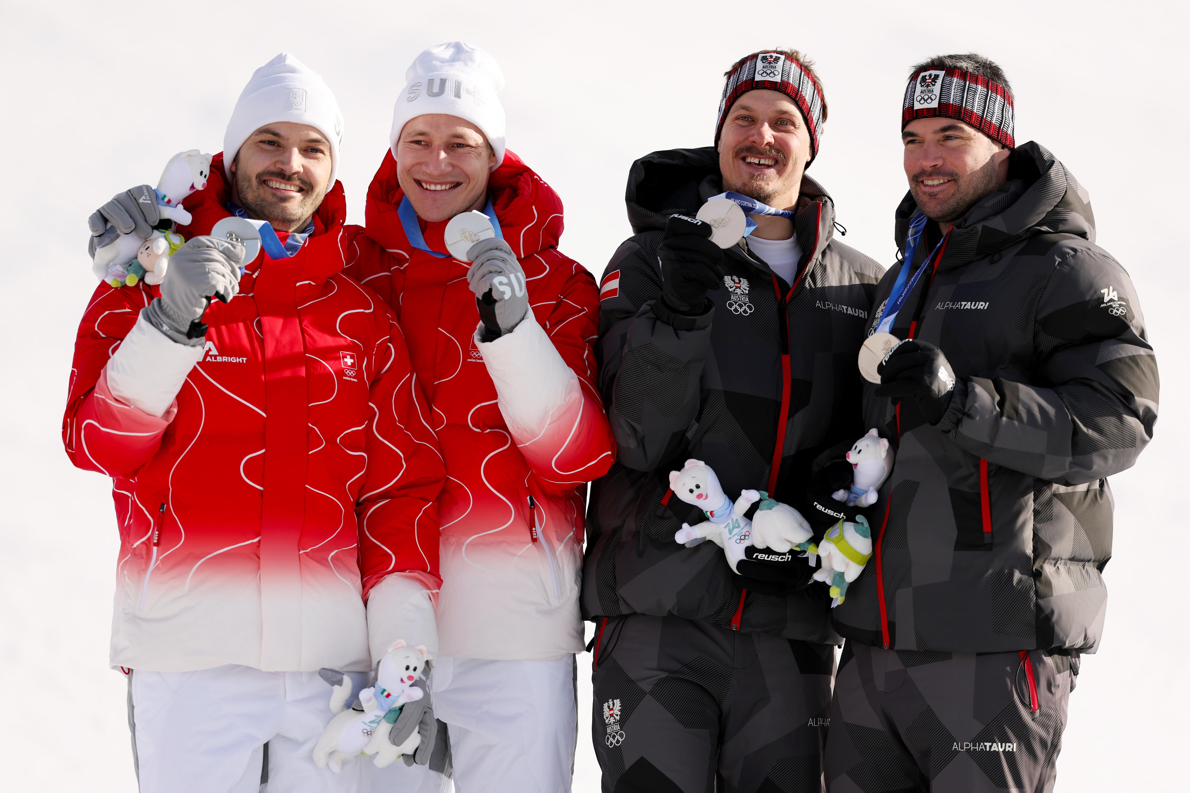 Quatro homens possuem medalhas de prata, dois com casacos vermelhos e dois com casacos pretos.