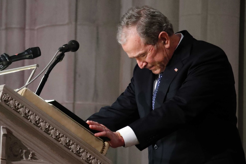 Former US President George W Bush bows his head while standing at a lectern.