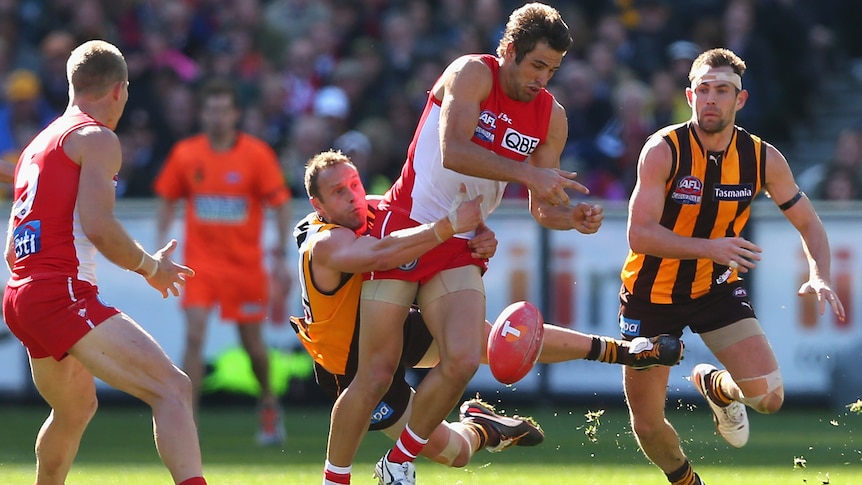 Josh Kennedy of the Swans handballs whilst being tackled by Brad Sewell of the Hawks.