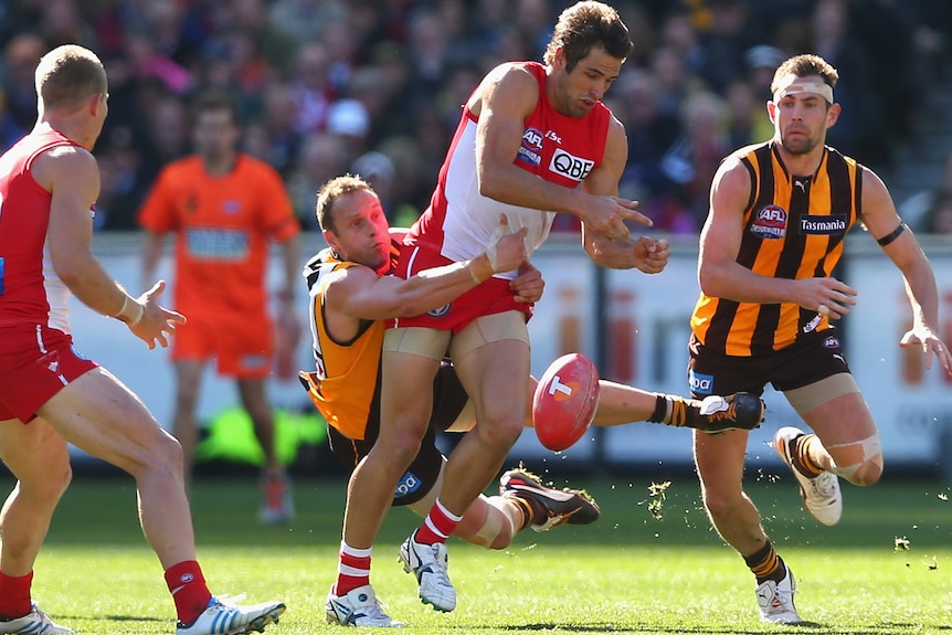 Josh Kennedy of the Swans handballs whilst being tackled by Brad Sewell of the Hawks.