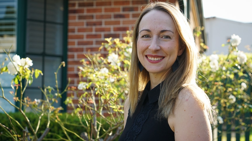 A woman smiles and stands in the garden, in a story about using energy accounting for anxiety and autism.