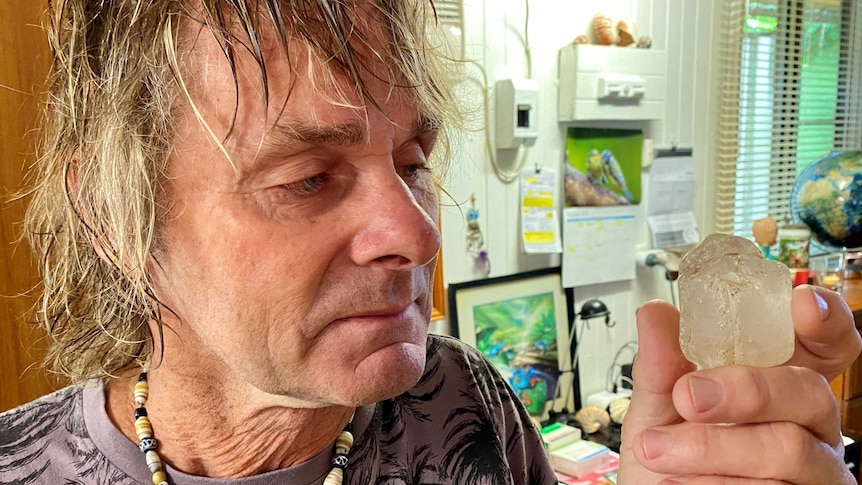 An older man with blonde hair looks at at a chunk of crystal.