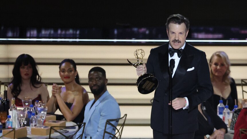 Jason Sudeikis holding an Emmy and wearing a suit on stage