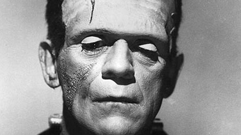 A black and white photo shows a forlorn man with theatrical makeup and skin grafts to make him look like Frankenstein.